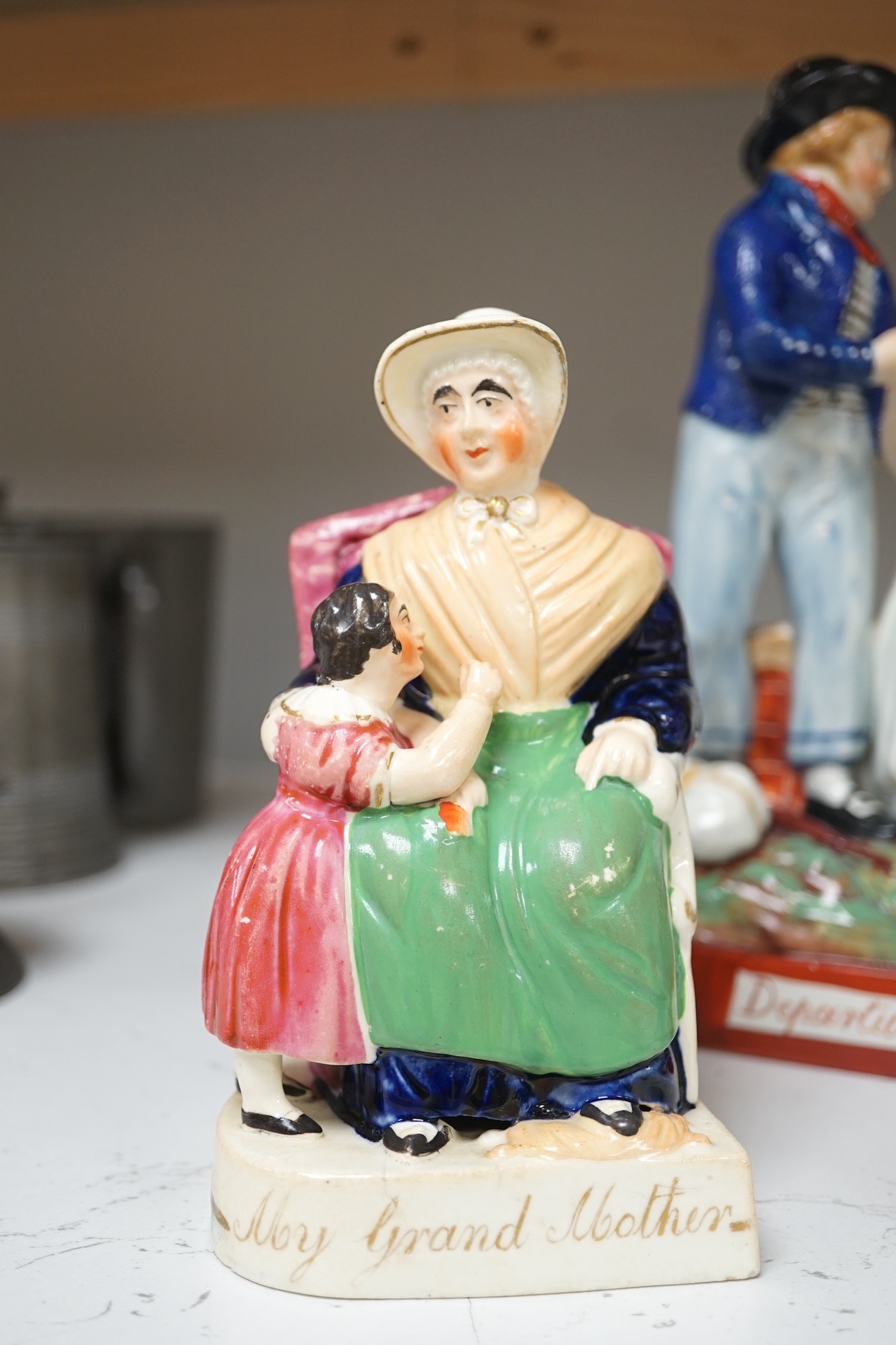 Six mid 19th century Staffordshire figures or groups: a pair titled ‘my grandmother and my grandfather’, a double sided water/gin figure, a pair of figural spill vases and a pearlware group titled ‘Departure’, the talles